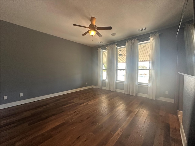 spare room featuring ceiling fan, visible vents, baseboards, and dark wood-style floors