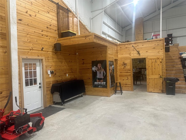 interior space featuring high vaulted ceiling, concrete floors, and wood walls