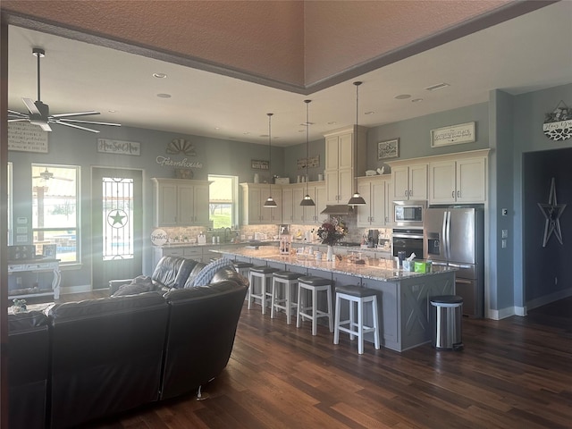 kitchen featuring a breakfast bar area, light stone counters, decorative backsplash, appliances with stainless steel finishes, and dark wood-style flooring