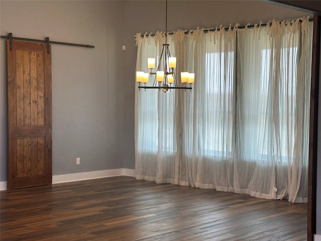 empty room with dark wood finished floors, an inviting chandelier, a barn door, and baseboards