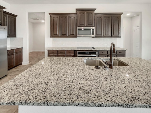 kitchen featuring a sink, decorative backsplash, light stone countertops, and appliances with stainless steel finishes