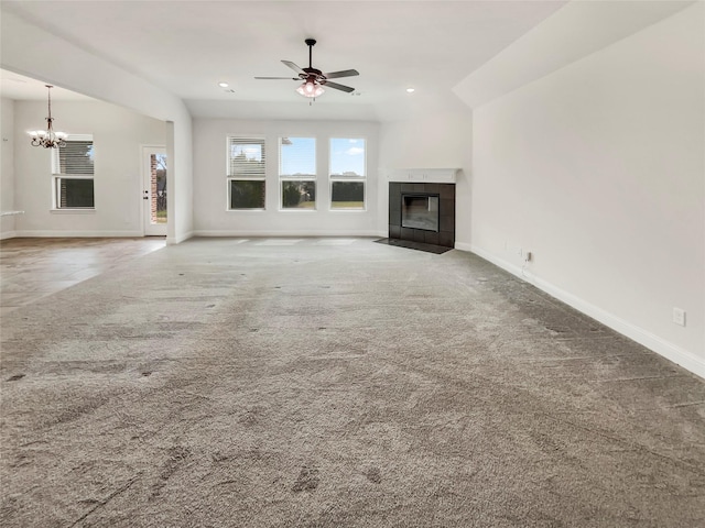 unfurnished living room with baseboards, a fireplace, carpet flooring, and ceiling fan with notable chandelier