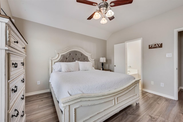 bedroom featuring a ceiling fan, wood finished floors, baseboards, vaulted ceiling, and connected bathroom