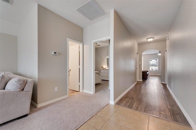 hallway featuring visible vents, arched walkways, carpet flooring, and tile patterned flooring