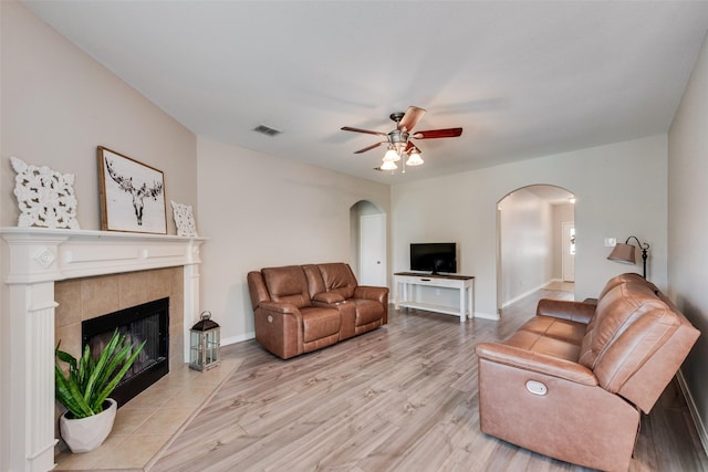 living room with visible vents, light wood-style flooring, arched walkways, a fireplace, and baseboards