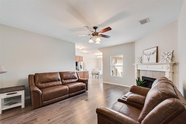 living room featuring visible vents, ceiling fan, baseboards, a fireplace, and wood finished floors