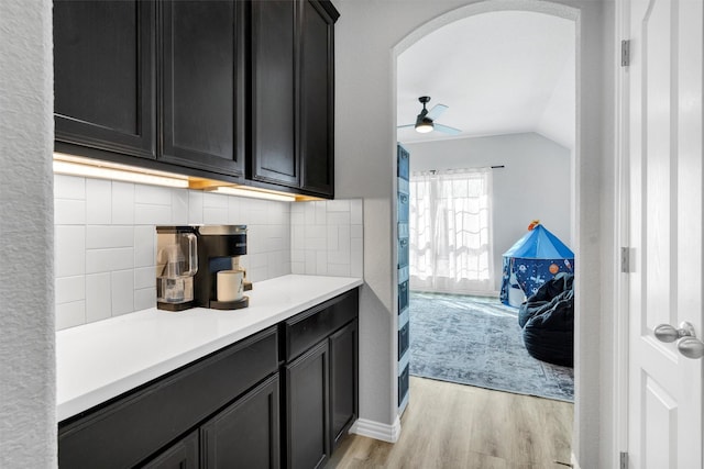 kitchen with tasteful backsplash, dark cabinets, light countertops, and light wood finished floors