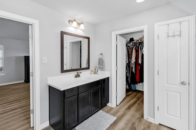 bathroom featuring vanity, a walk in closet, wood finished floors, and baseboards