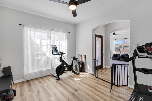 workout area with arched walkways, light wood-style flooring, a ceiling fan, and baseboards