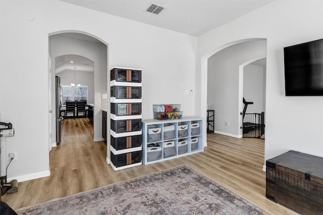 corridor with arched walkways, visible vents, a notable chandelier, and wood finished floors