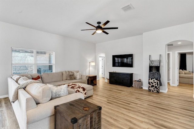 living area with visible vents, baseboards, arched walkways, ceiling fan, and light wood-style floors