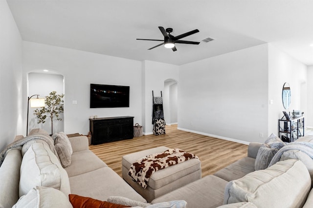 living area featuring visible vents, baseboards, light wood-style flooring, arched walkways, and a ceiling fan