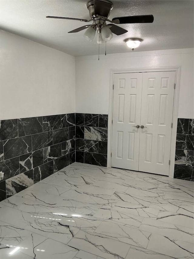 unfurnished bedroom featuring a closet, a textured ceiling, marble finish floor, and a ceiling fan