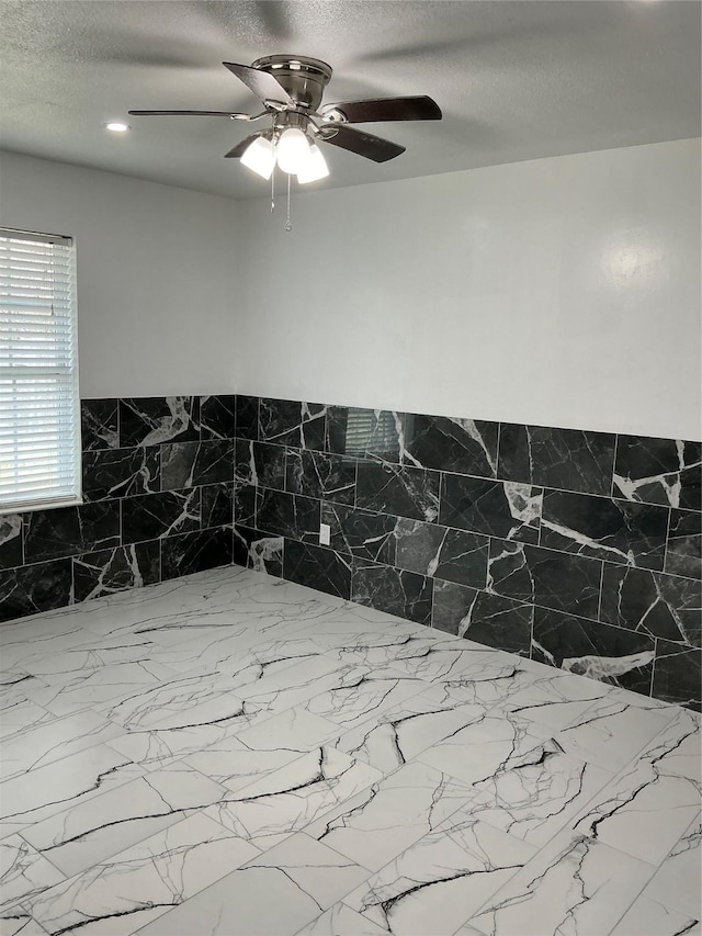 unfurnished bedroom featuring ceiling fan, tile walls, and a textured ceiling