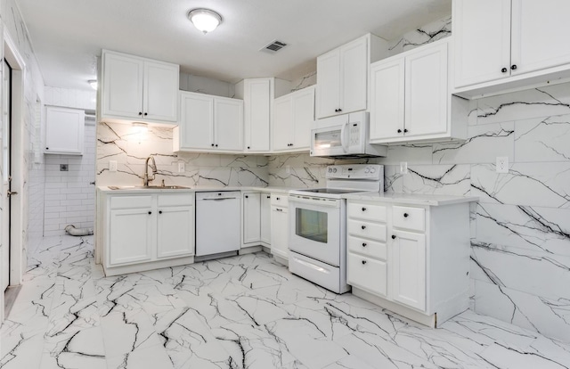 kitchen with white appliances, visible vents, a sink, white cabinets, and tasteful backsplash