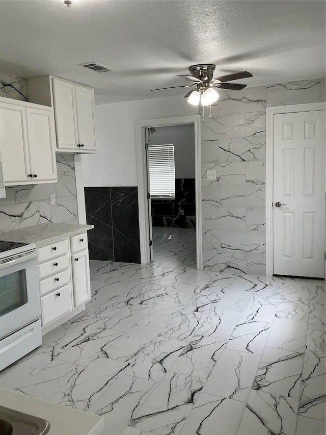 kitchen featuring visible vents, white range with electric cooktop, a textured ceiling, white cabinets, and ceiling fan