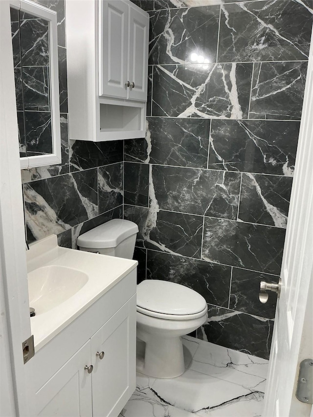 bathroom featuring marble finish floor, vanity, tile walls, and toilet