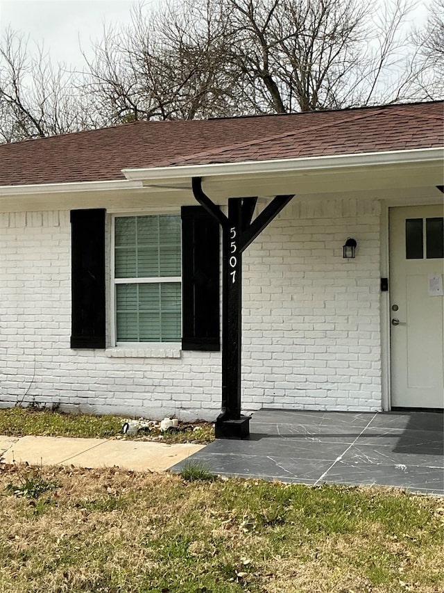 doorway to property with brick siding and a shingled roof