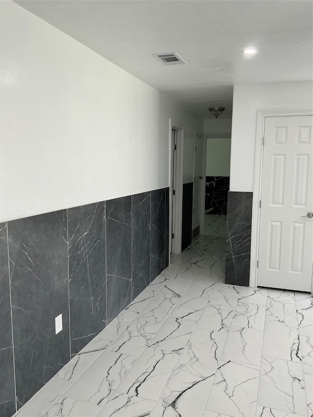 unfurnished room featuring visible vents, tile walls, and a wainscoted wall