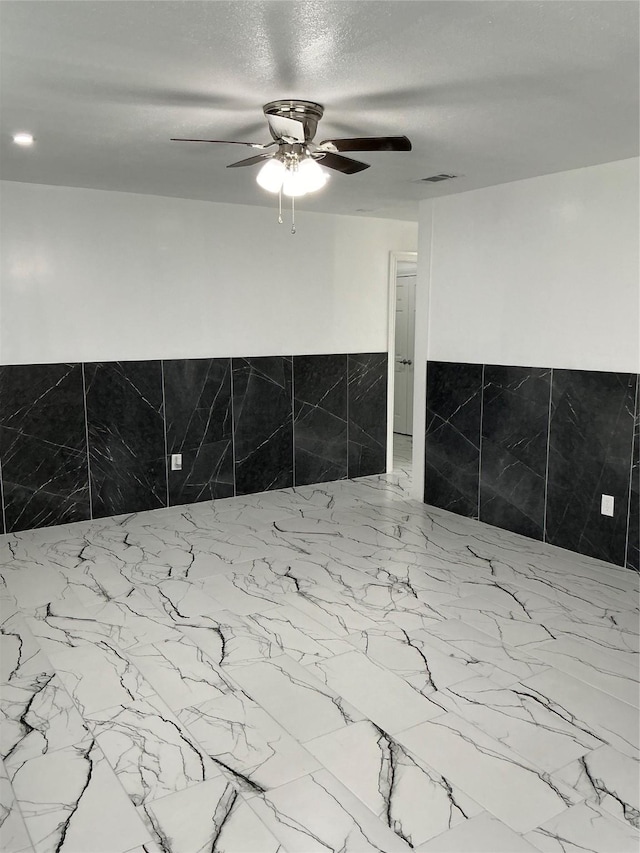 interior details with visible vents, a textured ceiling, wainscoting, and a ceiling fan