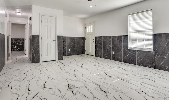 spare room featuring marble finish floor, wainscoting, and a ceiling fan