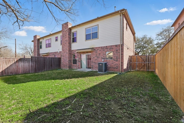 back of property featuring a yard, a fenced backyard, central AC, a chimney, and brick siding