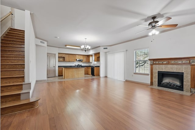 unfurnished living room featuring visible vents, ceiling fan with notable chandelier, stairway, crown molding, and light wood finished floors