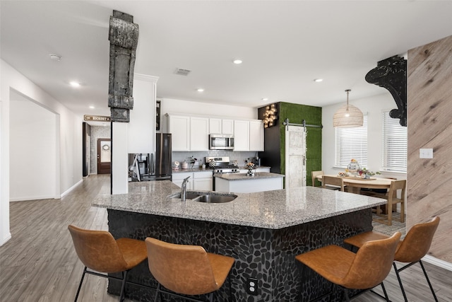 kitchen with a kitchen island with sink, a sink, appliances with stainless steel finishes, a barn door, and a kitchen breakfast bar