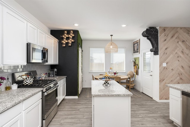 kitchen with a kitchen island, light wood-style flooring, stainless steel appliances, white cabinetry, and backsplash