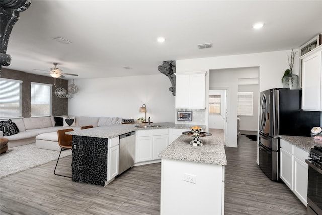 kitchen featuring visible vents, open floor plan, a peninsula, stainless steel appliances, and a sink