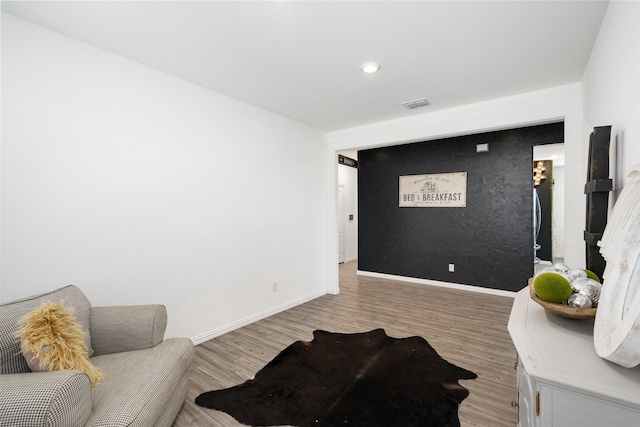 living area featuring visible vents, baseboards, light wood-style floors, and an accent wall