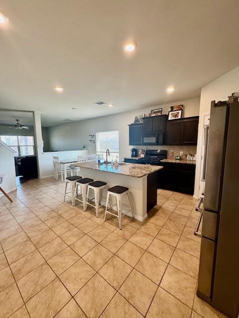 kitchen with a breakfast bar, black appliances, a center island with sink, a sink, and light tile patterned flooring