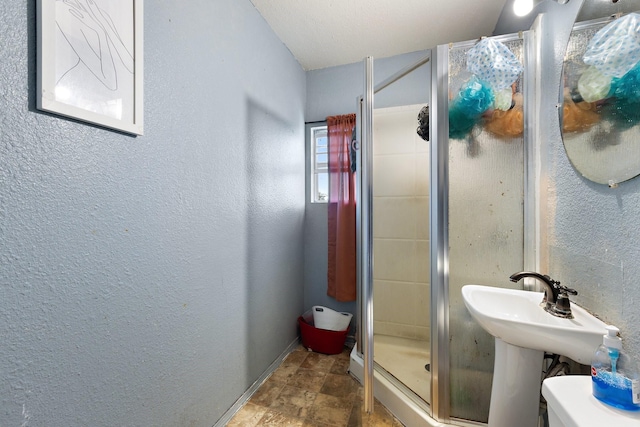 full bath featuring baseboards, a textured wall, a stall shower, and stone finish flooring