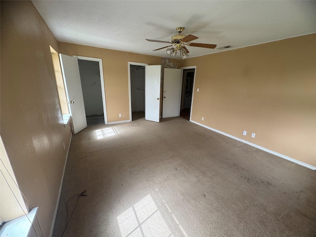 unfurnished bedroom featuring visible vents, two closets, baseboards, a textured ceiling, and a ceiling fan