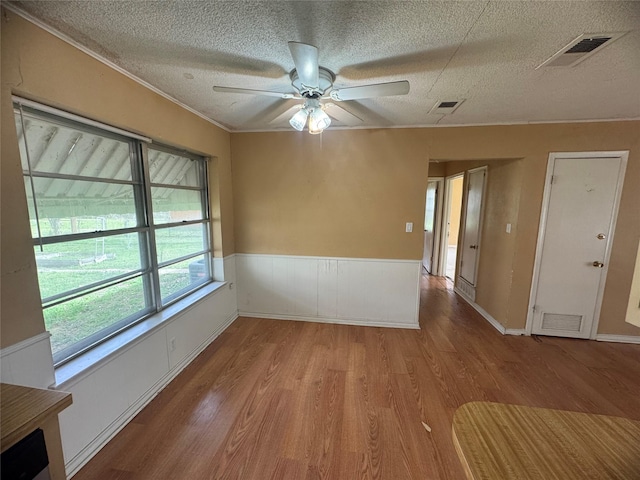 empty room with wood finished floors, visible vents, and wainscoting