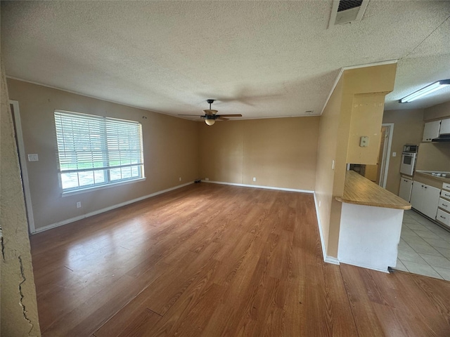 unfurnished living room with visible vents, baseboards, light wood-style flooring, a textured ceiling, and a ceiling fan