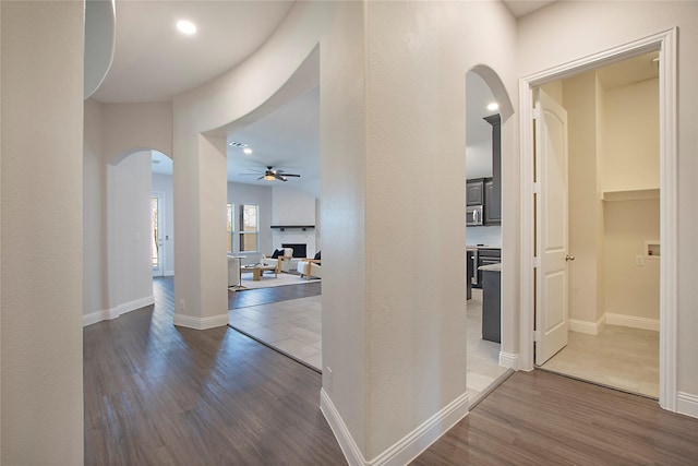 corridor featuring dark wood-type flooring, baseboards, and arched walkways