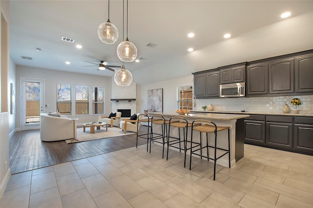 kitchen featuring a kitchen bar, stainless steel microwave, open floor plan, and visible vents