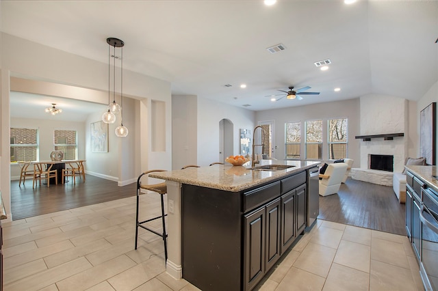 kitchen featuring a sink, stainless steel dishwasher, arched walkways, a fireplace, and light stone countertops