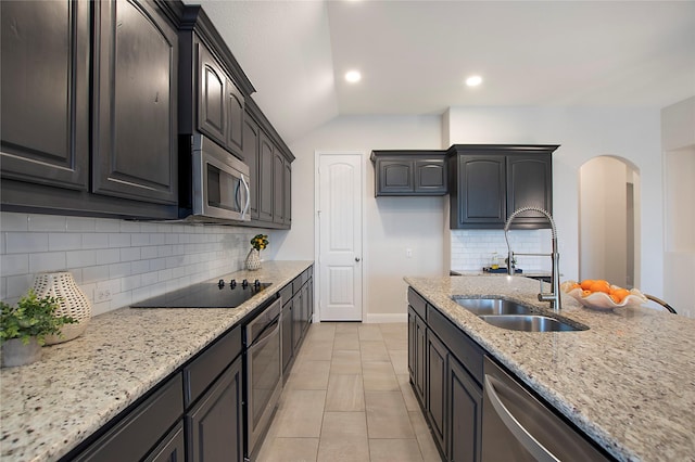 kitchen with light stone countertops, recessed lighting, appliances with stainless steel finishes, arched walkways, and a sink