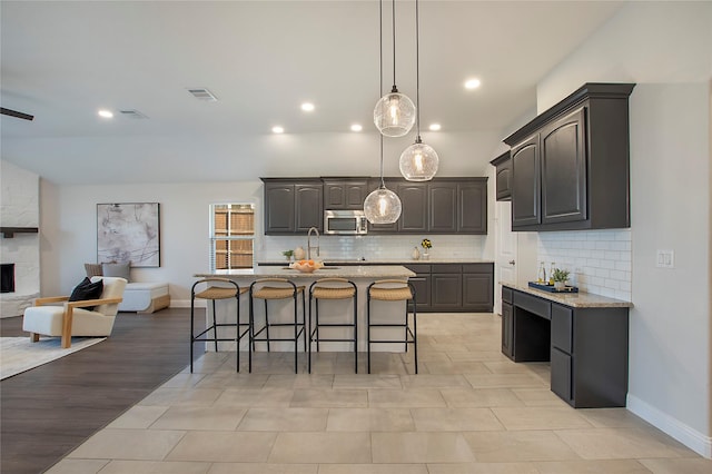 kitchen featuring tasteful backsplash, stainless steel microwave, visible vents, open floor plan, and a kitchen bar