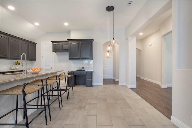 kitchen with a sink, a kitchen breakfast bar, tasteful backsplash, baseboards, and light stone countertops