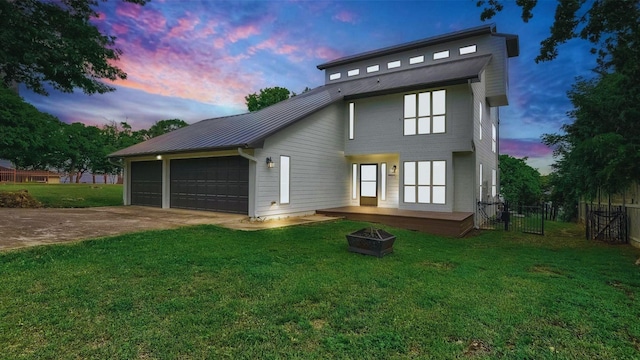 back of house at dusk featuring a yard, fence, a garage, and an outdoor fire pit