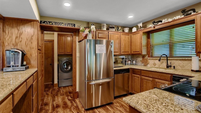 kitchen with wood finished floors, washer / dryer, a sink, decorative backsplash, and stainless steel appliances