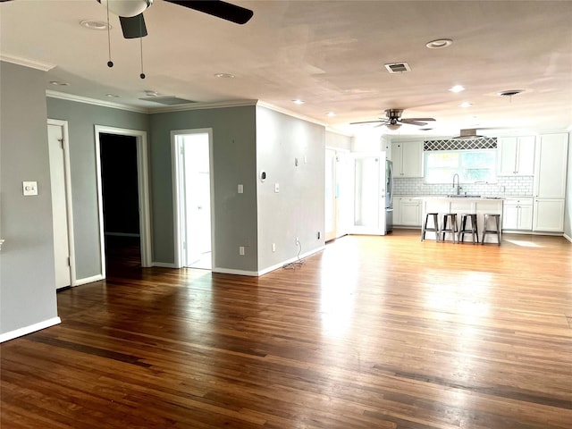 unfurnished living room with visible vents, wood finished floors, crown molding, and a sink