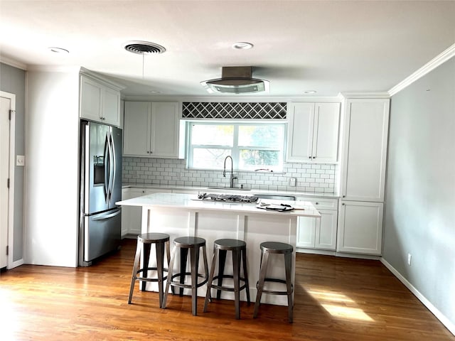 kitchen with wood finished floors, light countertops, a kitchen breakfast bar, stainless steel fridge, and a center island