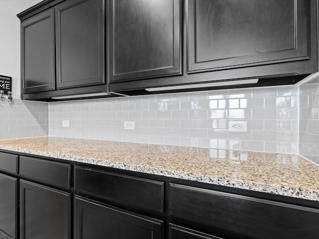 kitchen with dark cabinetry, light stone countertops, and tasteful backsplash