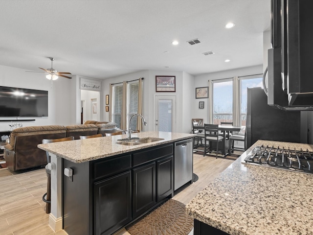 kitchen with visible vents, an island with sink, a sink, dark cabinetry, and appliances with stainless steel finishes