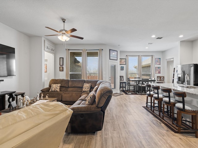 living area featuring light wood-type flooring, visible vents, a textured ceiling, recessed lighting, and ceiling fan