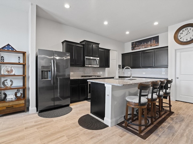 kitchen with wood tiled floor, dark cabinets, light stone counters, stainless steel appliances, and a sink